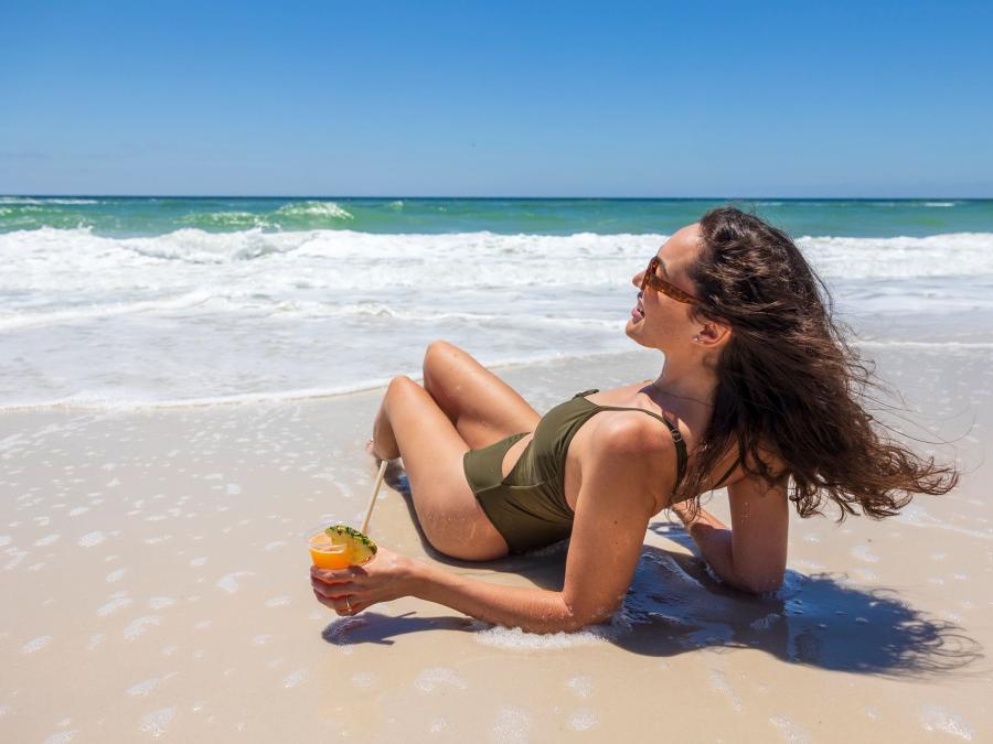 Woman lounging on the beach with a drink in hand in Gulf Shores